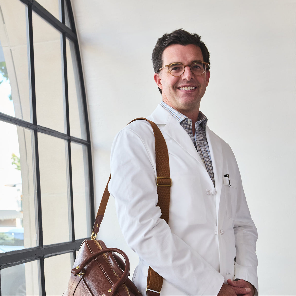 Man in a white coat with a brown bag standing indoors.